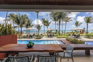 A poolside area with a view of the ocean, palm trees, and outdoor seating. - Porto Beach Residence (Ipojuca)