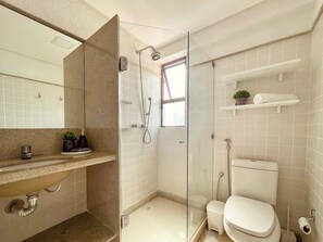 A bathroom with a glass-enclosed shower, a toilet, a sink with a mirror, and a small shelf with a plant. - Porto Beach Residence (Ipojuca)