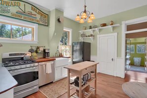 A kitchen with a stove, refrigerator, and wooden table. - Bohemian Dream Hot Tub Bike Downtown Fire pit (Colorado Springs)
