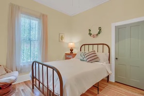 A bedroom with a bed, a nightstand, a lamp, a chair, a window with curtains, and a door. - Bohemian Dream Hot Tub Bike Downtown Fire pit (Colorado Springs)