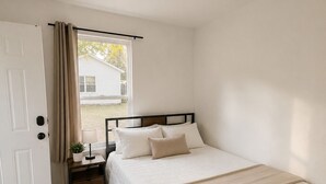 A bedroom with a bed, bedside table, lamp, and a window with curtains. - Private Studio in North Austin ~ Near The Domain, AC & Free Parking (Austin)