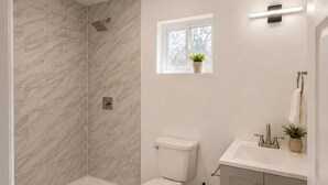 A modern bathroom with a shower, toilet, and sink, featuring marble tiles and a small window with a plant. - Private Studio in North Austin ~ Near The Domain, AC & Free Parking (Austin)