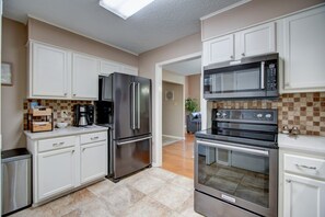 Una cocina moderna con electrodomésticos de acero inoxidable, armarios blancos y salpicadero de azulejos.