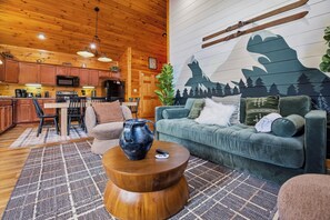A cozy living room with a sofa, a coffee table, and a kitchen area in the background. - MT Views Cozy, Well Appointed Hot Tub + Game Room, 1.5 Mi to Downtown, Sleeps 10 (Gatlinburg)