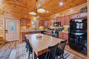 A wooden cabin interior with a large dining table, kitchen area, and a refrigerator. - MT Views Cozy, Well Appointed Hot Tub + Game Room, 1.5 Mi to Downtown, Sleeps 10 (Gatlinburg)