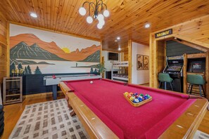 A pool table with a red felt surface, a billiards cue, and a rack of billiard balls. - MT Views Cozy, Well Appointed Hot Tub + Game Room, 1.5 Mi to Downtown, Sleeps 10 (Gatlinburg)