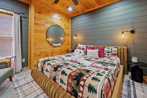 A cozy bedroom with a wooden ceiling, a round mirror, a bed with a quilt, bedside lamps, and a small table with a plant. - MT Views Cozy, Well Appointed Hot Tub + Game Room, 1.5 Mi to Downtown, Sleeps 10 (Gatlinburg)