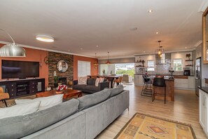 A modern living room with a large grey sofa, a flat-screen TV, and a stone wall. - Villa Azure, Vermont Home with Studio, Mountain & Sea Views (Vermont)