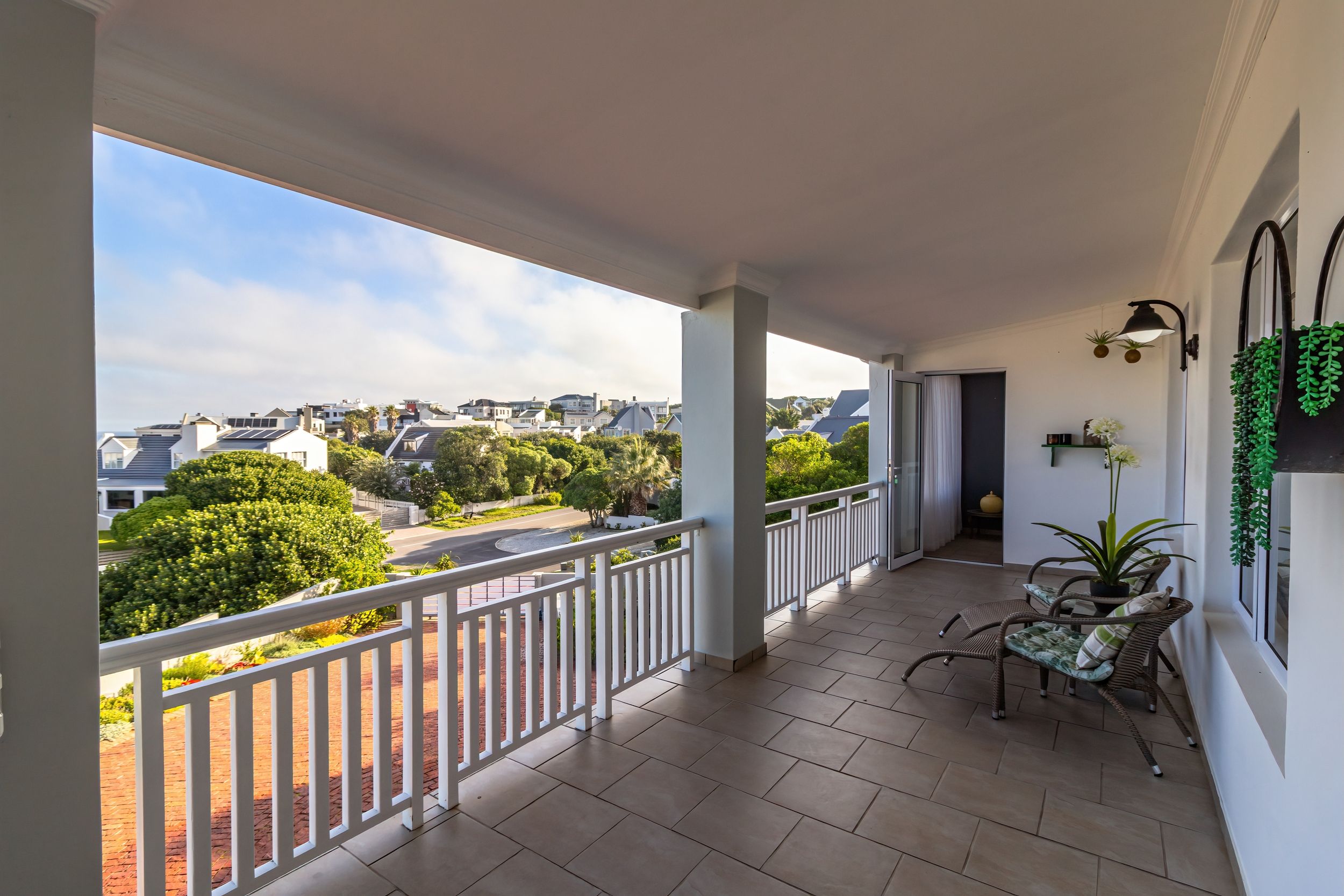 Een balkon met uitzicht op een woonwijk, een plant in pot en een zithoek.