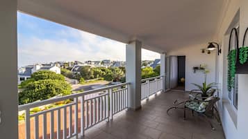 Een balkon met uitzicht op een woonwijk, een plant in pot en een zithoek.