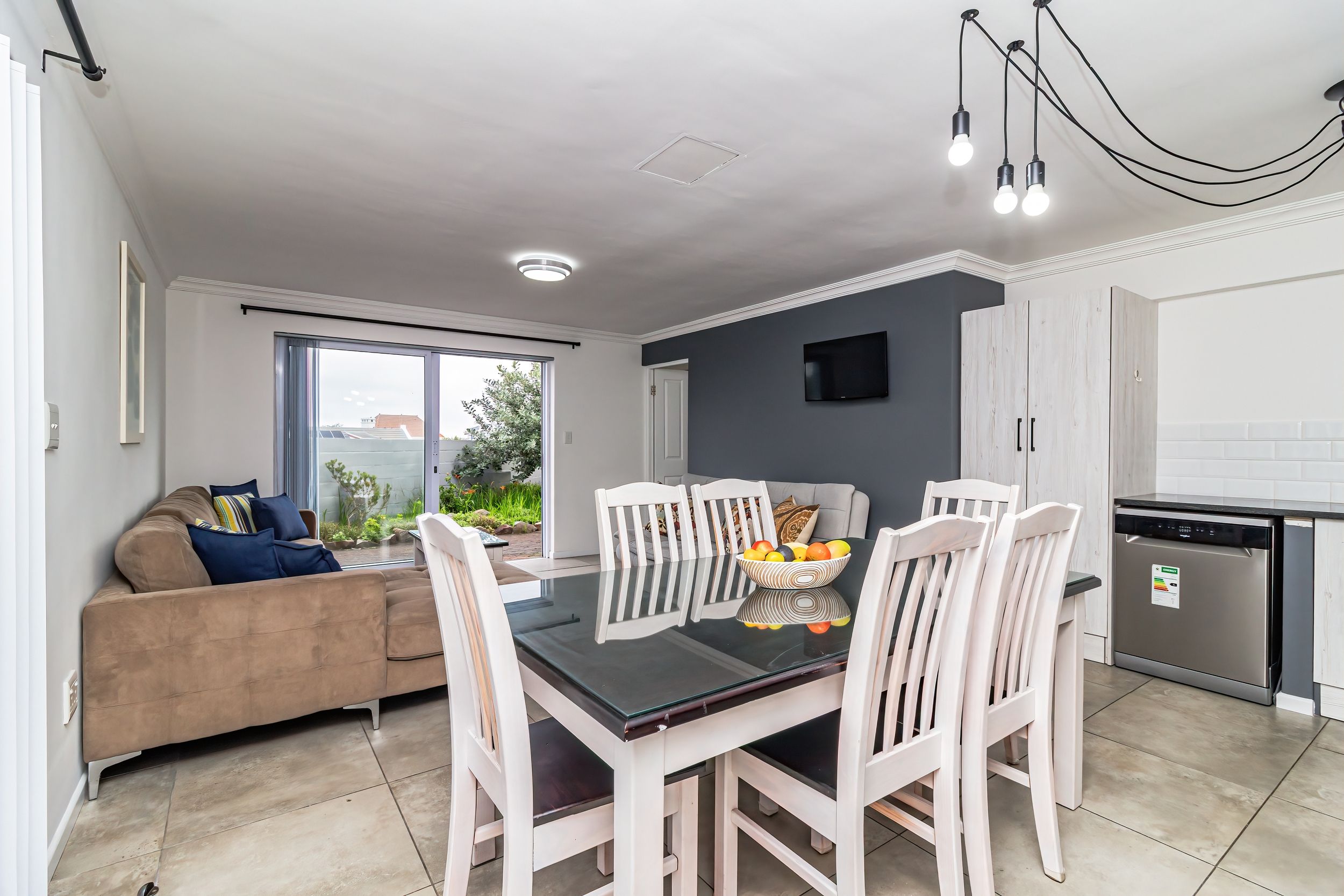 A modern kitchen with a dining area, a sofa, and a TV mounted on the wall.