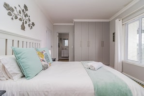 A bedroom with a bed, pillows, a bedside table, a wardrobe, and a window with blinds. - Villa Azure, Vermont Home with Studio, Mountain & Sea Views (Vermont)