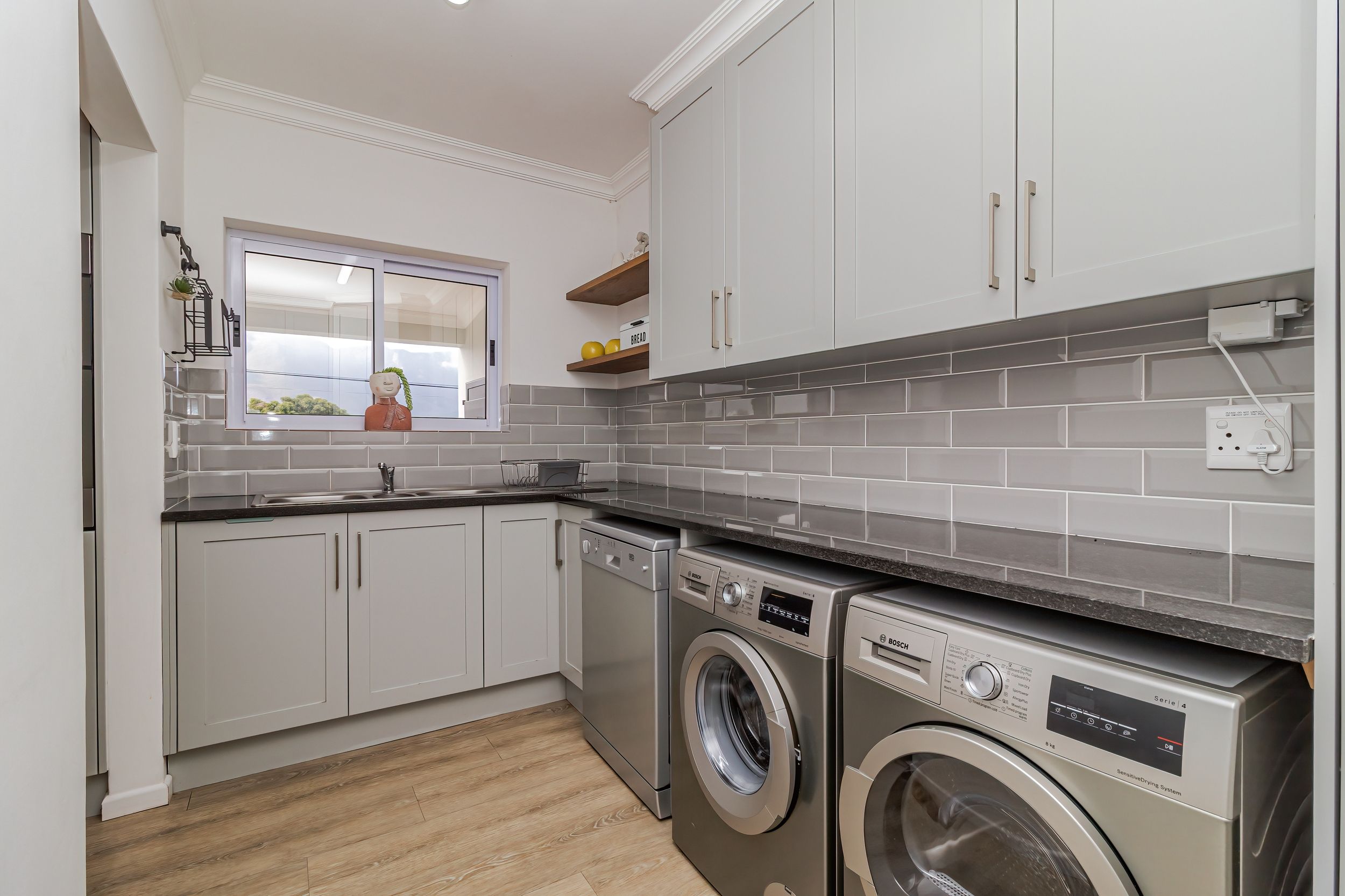 A modern kitchen with white cabinets, a built-in washing machine, and a window with a view.