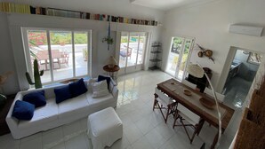 A spacious living area with a white sofa, a dining table, and a bookshelf filled with books. - "Pinetina" Beach Villa (Palermo)