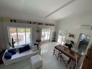 A spacious living area with a white sofa, a dining table, and a bookshelf filled with books. - "Pinetina" Beach Villa (Palermo)