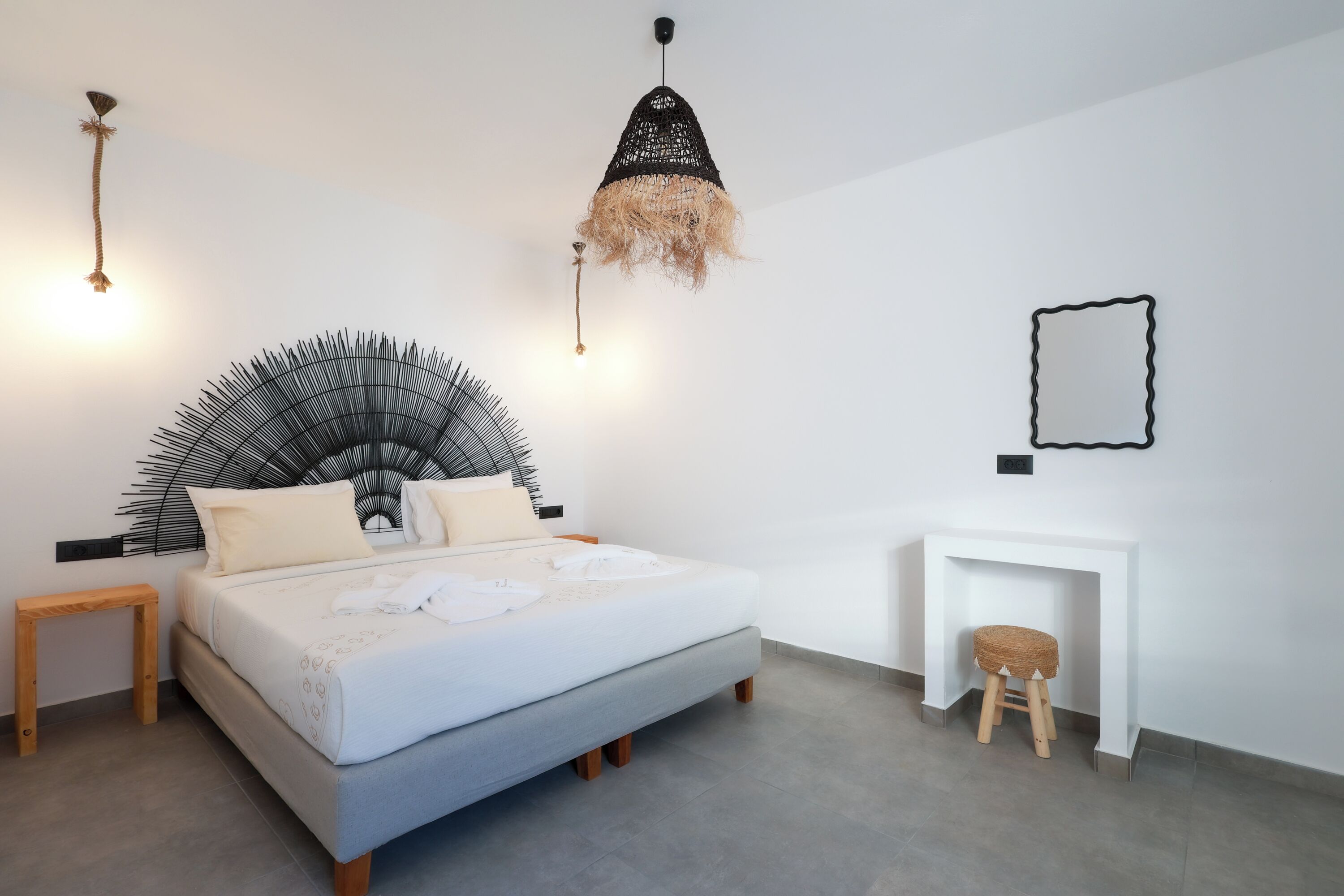 Une chambre à coucher moderne avec un lit, des tables de chevet, un luminaire suspendu, un miroir et un petit tabouret.