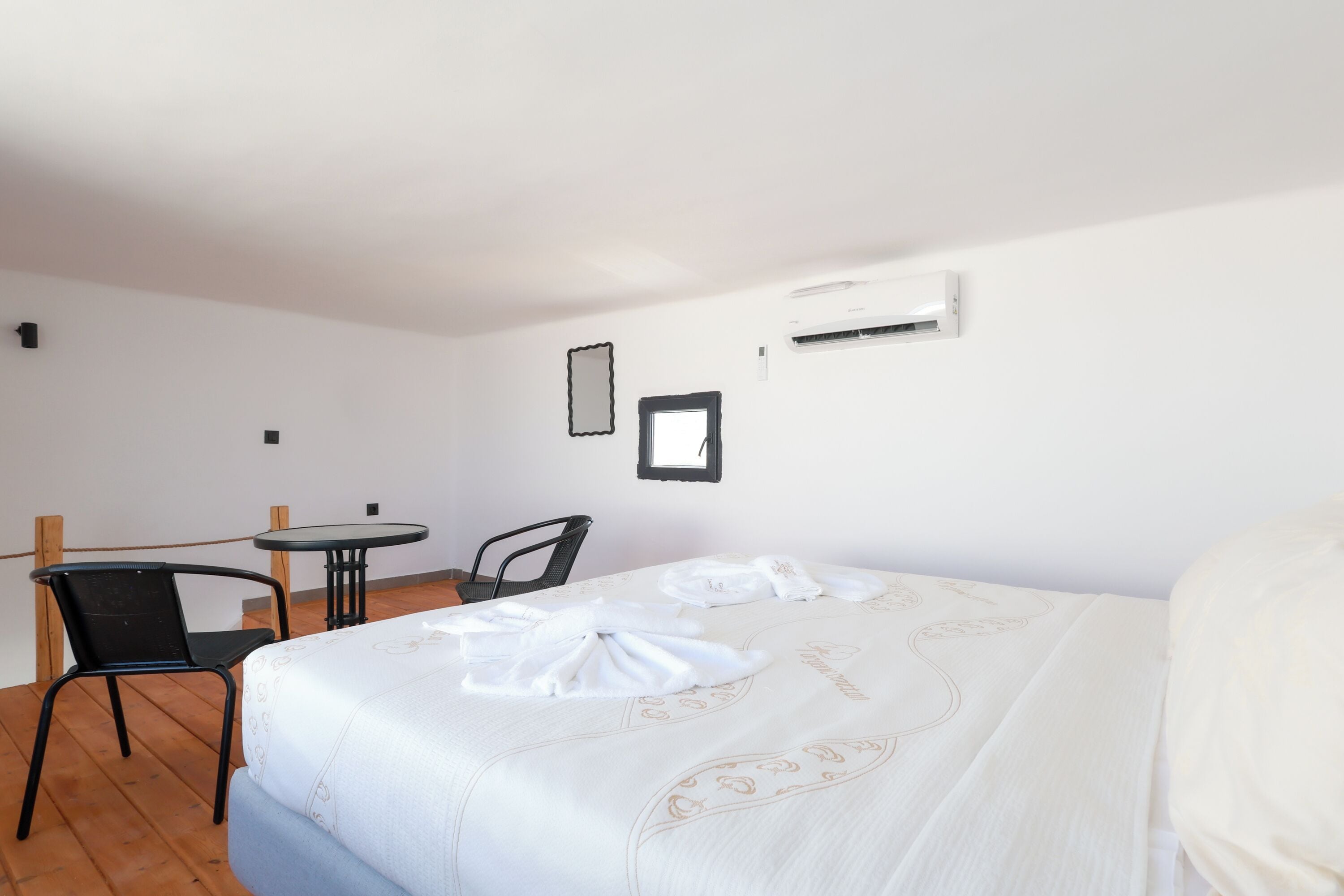 Habitación de hotel con cama, una mesita, dos sillas y un equipo de aire acondicionado en la pared.