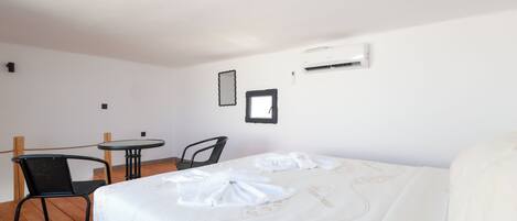 Habitación de hotel con cama, una mesita, dos sillas y un equipo de aire acondicionado en la pared.