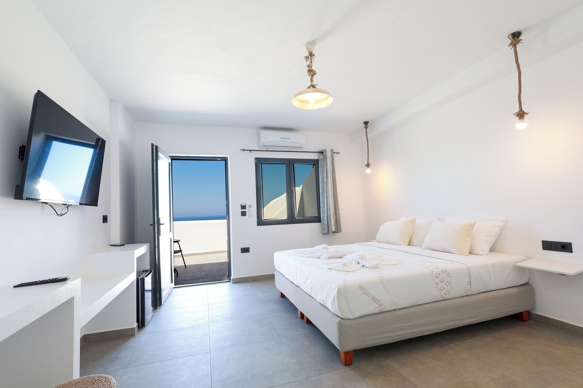 Un dormitorio con cama, escritorio, televisión y balcón.