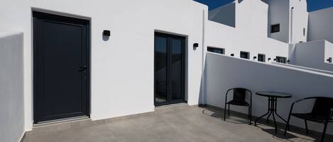 Un edificio moderno con puerta negra, puerta de vidrio y un pequeño espacio al aire libre con dos sillas y una mesa.
