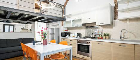 Une cuisine moderne avec des meubles blancs, une table à manger avec des chaises orange et un four visible.