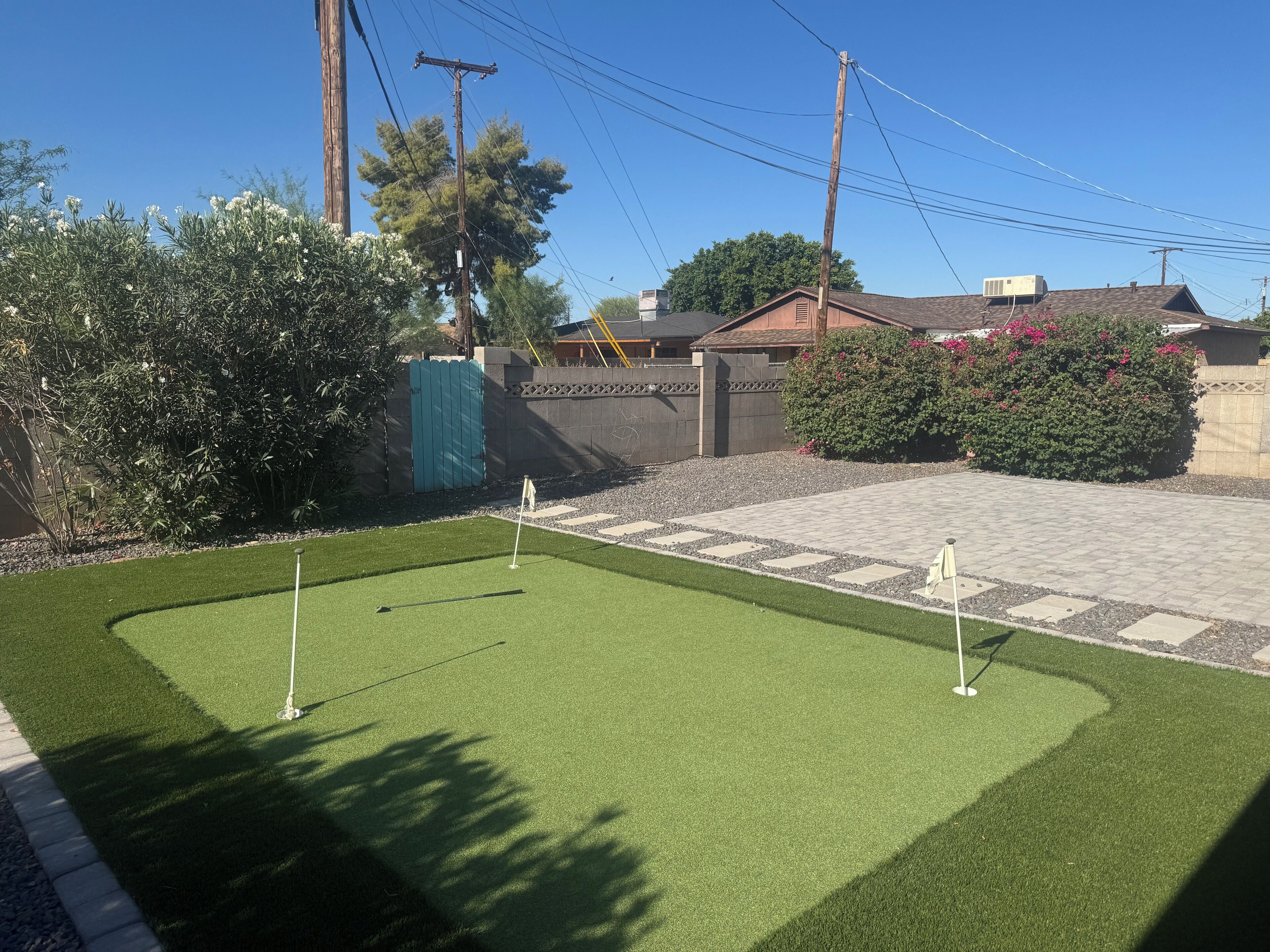 A well-maintained lawn with two golf holes, a paved walkway, and a residential setting with a house and a green fence.