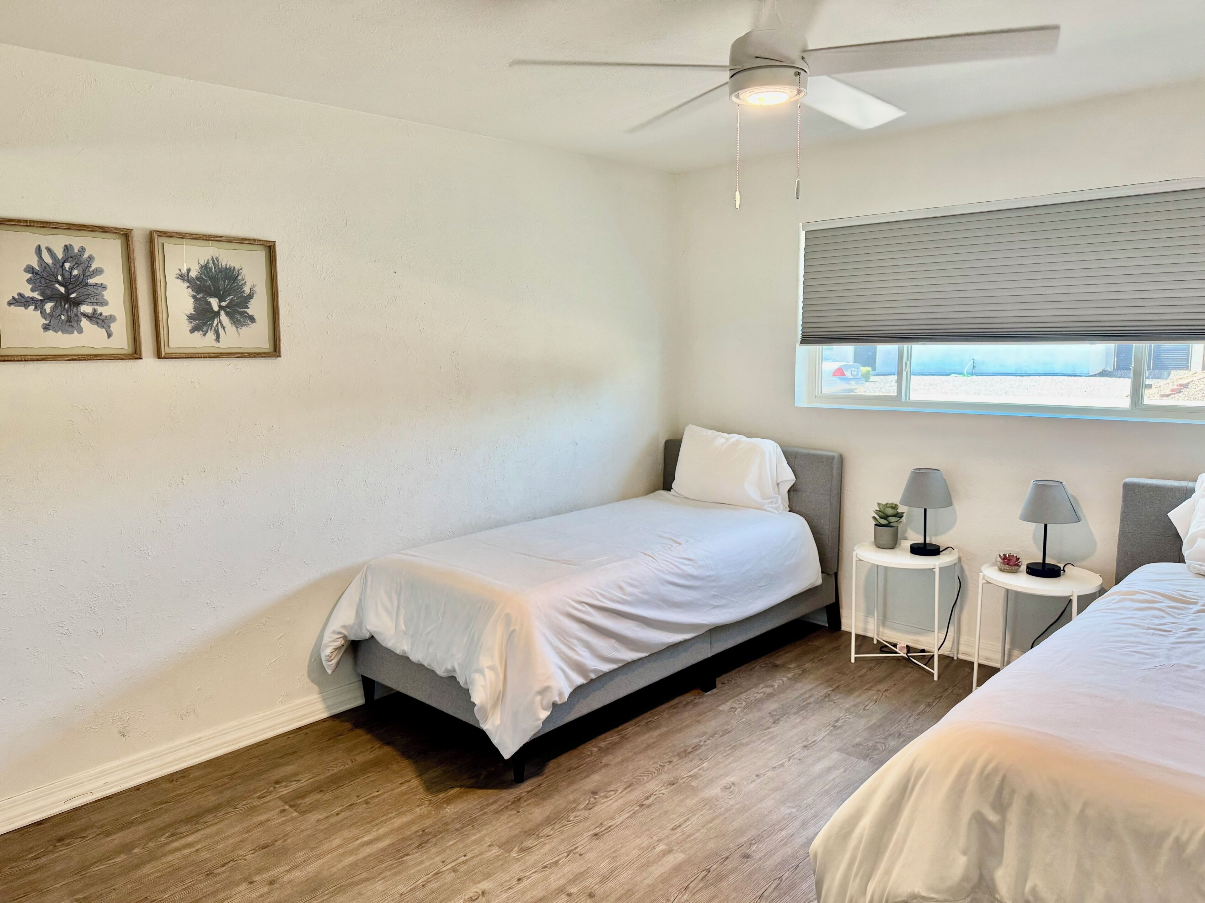 Une chambre à coucher comprenant un lit, un ventilateur de plafond, une fenêtre avec des stores et deux tables de chevet avec des lampes.