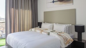 Ein modernes Hotelzimmer mit einem großen Bett, einem Nachttisch, einer Lampe, einem Bild an der Wand und Blick ins Freie.
