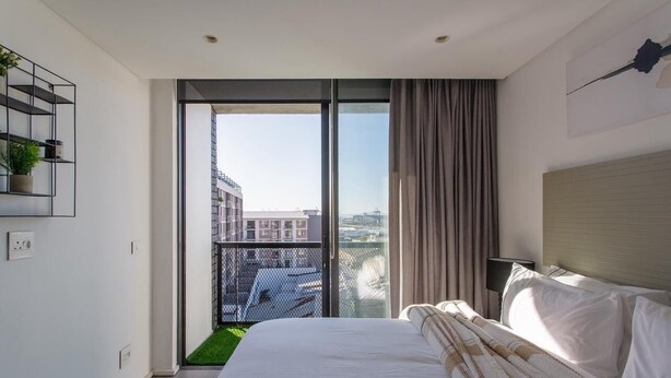 Ein modernes Hotelzimmer mit einem großen Bett, Blick auf die Stadt und einem Balkon mit Grünflächen.