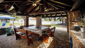 Un patio al aire libre con suelo de piedra, mobiliario de madera y una zona cubierta con ventilador de techo.