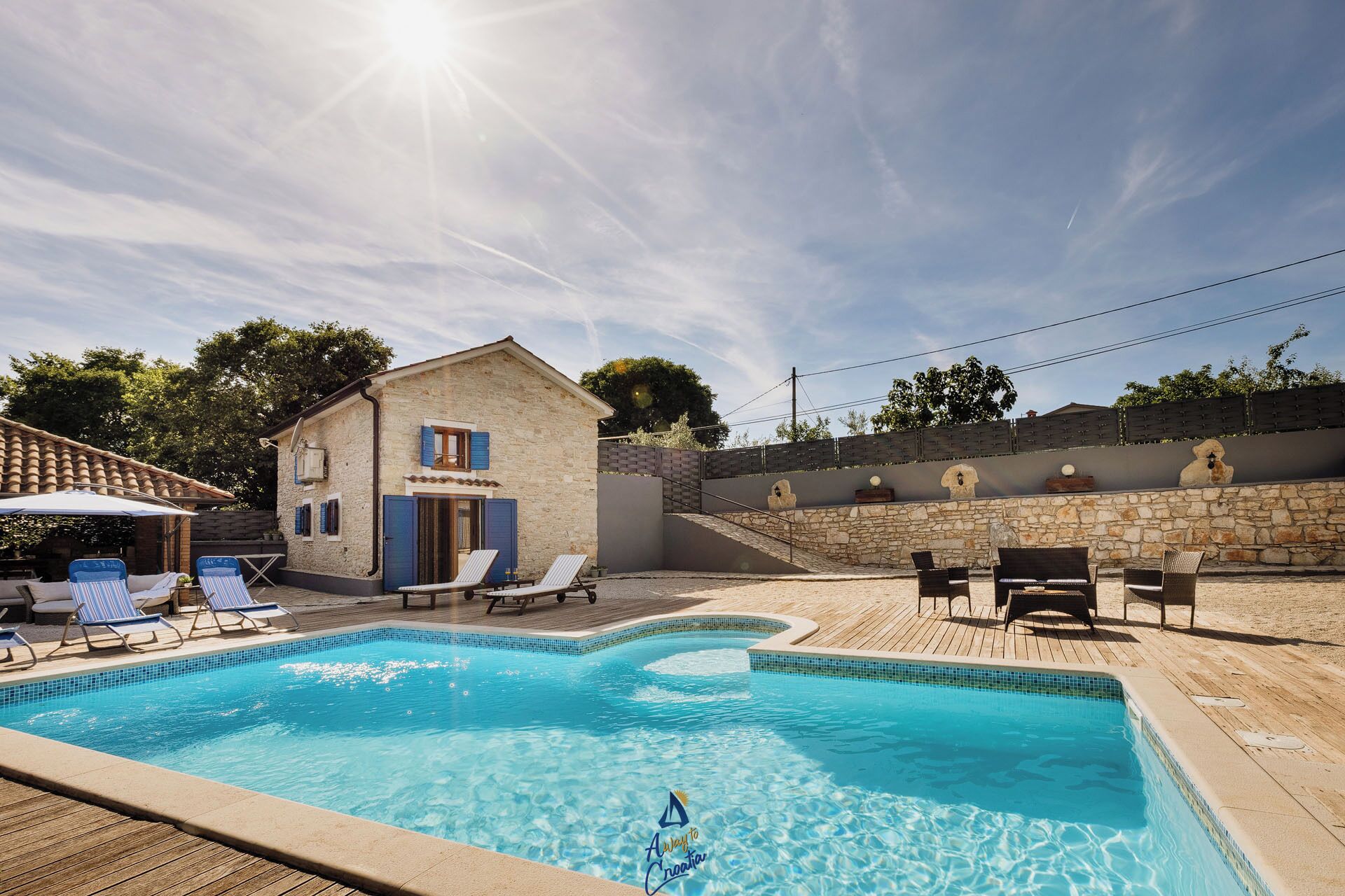 A swimming pool with lounge chairs, a stone building, and a wooden deck.