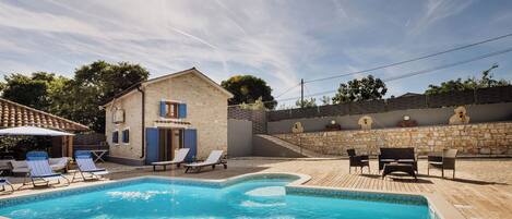 A swimming pool with lounge chairs, a stone building, and a wooden deck.