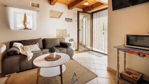 Una sala de estar con un sofá, una mesita redonda, un televisor y una puerta que da a un balcón.