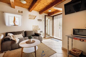 Ein Wohnzimmer mit einer Couch, einem kleinen runden Tisch, einem Fernseher und einer Tür, die auf einen Balkon führt.
