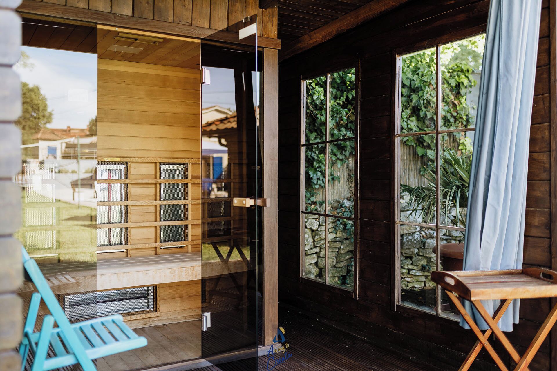 Eine Holzhütte mit einer Schiebetür, einer kleinen Veranda mit einer Bank und einem Fenster mit Blick auf Grünflächen.