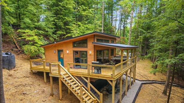 A wooden cabin with a deck, a staircase, and a small outdoor seating area.