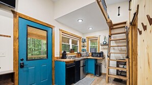 A modern kitchen with a blue door, wooden cabinets, and a central island. - Whitney Nook: The Ultimate Cozy & Connected Couples’ Hideaway (Campton)