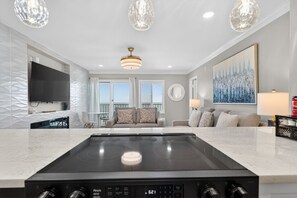 A modern kitchen with a built-in induction cooktop, a flat-screen TV, and a dining area with a table and chairs. - Beachfront Condo dr 1402 (Virginia Beach)