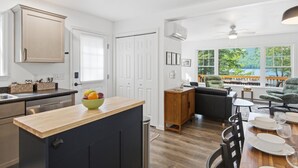 Een moderne keuken met een houten kookeiland, een eethoek met een tafel voor twee personen, en uitzicht op een meer door grote ramen.