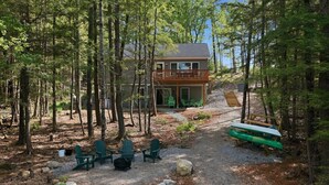Een chalet met terras, omringd door bomen, met buitenmeubels en een kano.