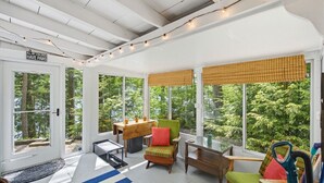Une véranda avec de grandes fenêtres, une table en bois, des chaises colorées et une pancarte sur laquelle on peut lire : « TOUS MES ENFANTS ONT DES PATTES ».