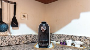 Keittiössä on kahvinkeitin, kaksi espressokuppia ja seinällä oleva lasta.