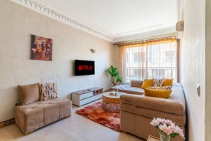 A living room with a sofa, a coffee table, a TV, and a plant. - Beautiful studio apartment in the heart of Guéliz: Wi-Fi, Netflix, parking (Marrakesh)