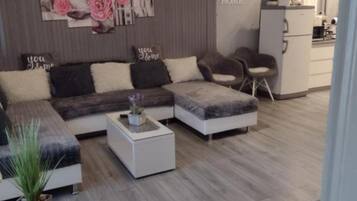 Un salon moderne avec un canapé d’angle, une petite table basse blanche et une plante en pot.