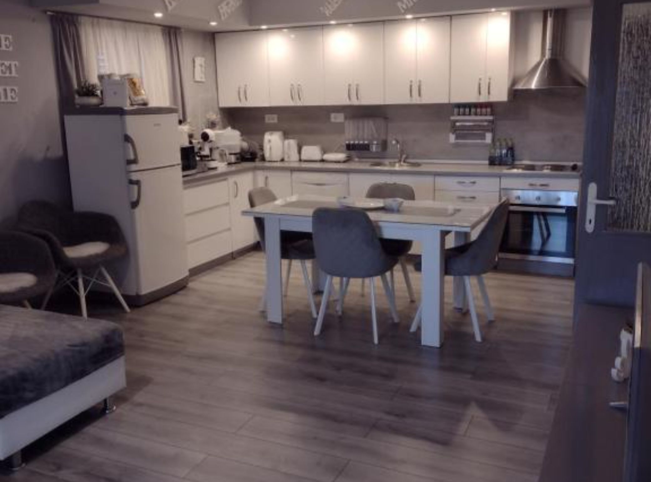 Une cuisine moderne avec des meubles blancs, une table à manger avec des chaises et un four encastré.