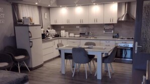 A modern kitchen with white cabinets, a dining table with chairs, and a built-in oven. - Mare`s Home (Sibenik)
