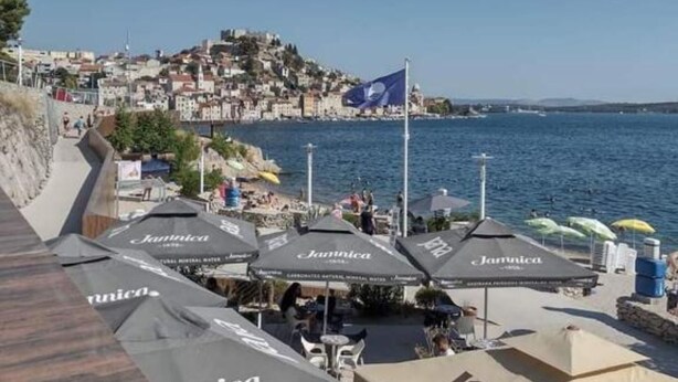 A coastal town with a view of the sea, a flag, and outdoor seating with umbrellas. - Mare`s Home (Sibenik)