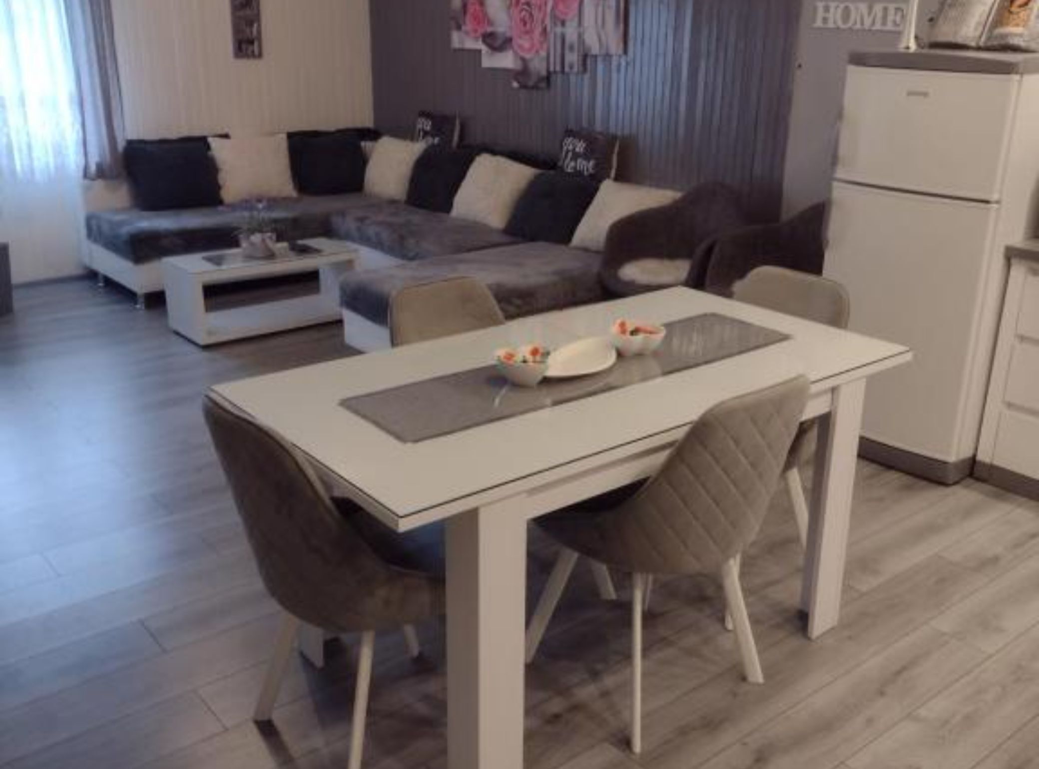 A modern living room with a sofa, a dining table with chairs, and a kitchen area.