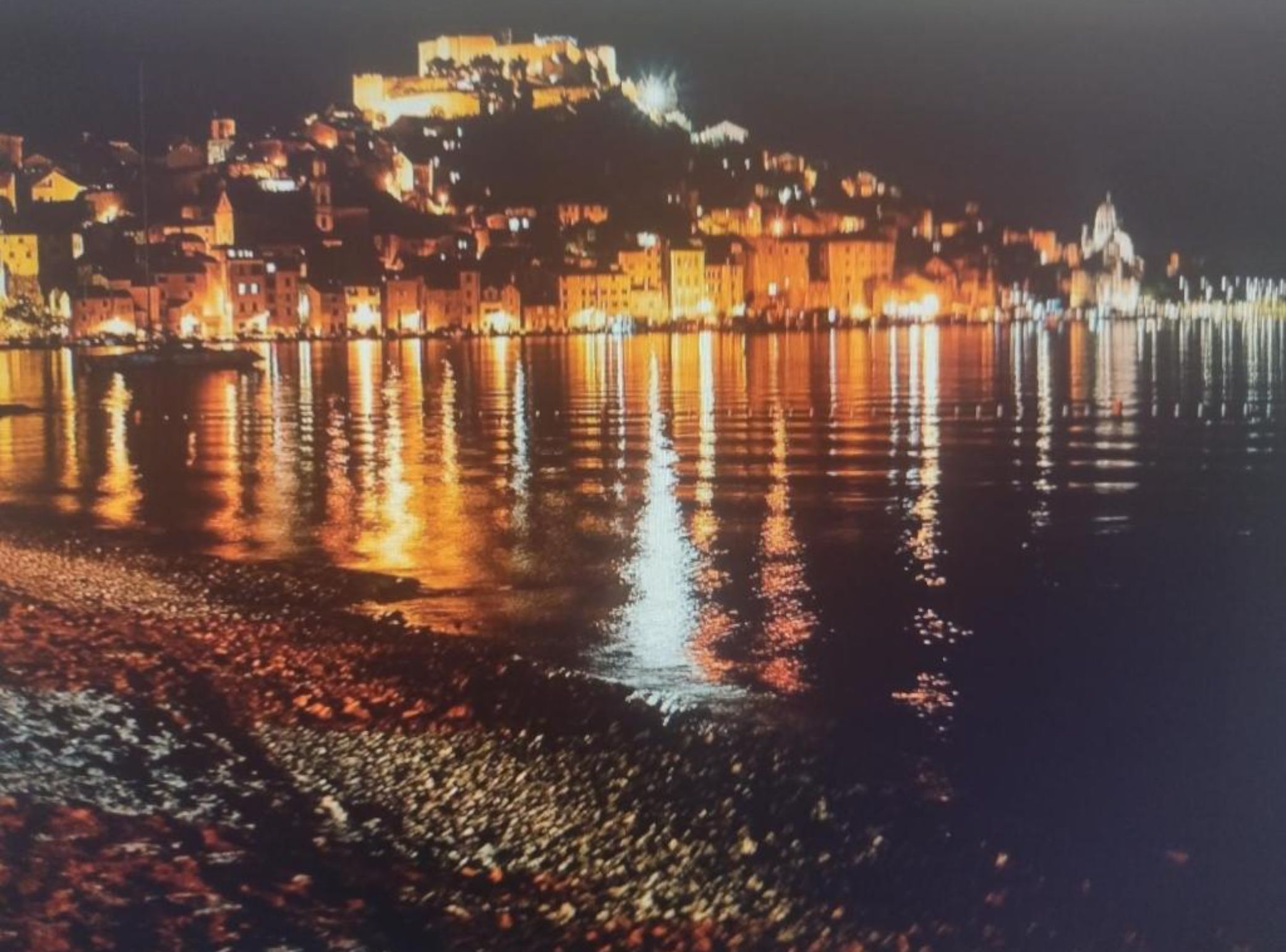 Une vue nocturne d’une ville, avec des bâtiments illuminés qui se reflètent sur l’eau.