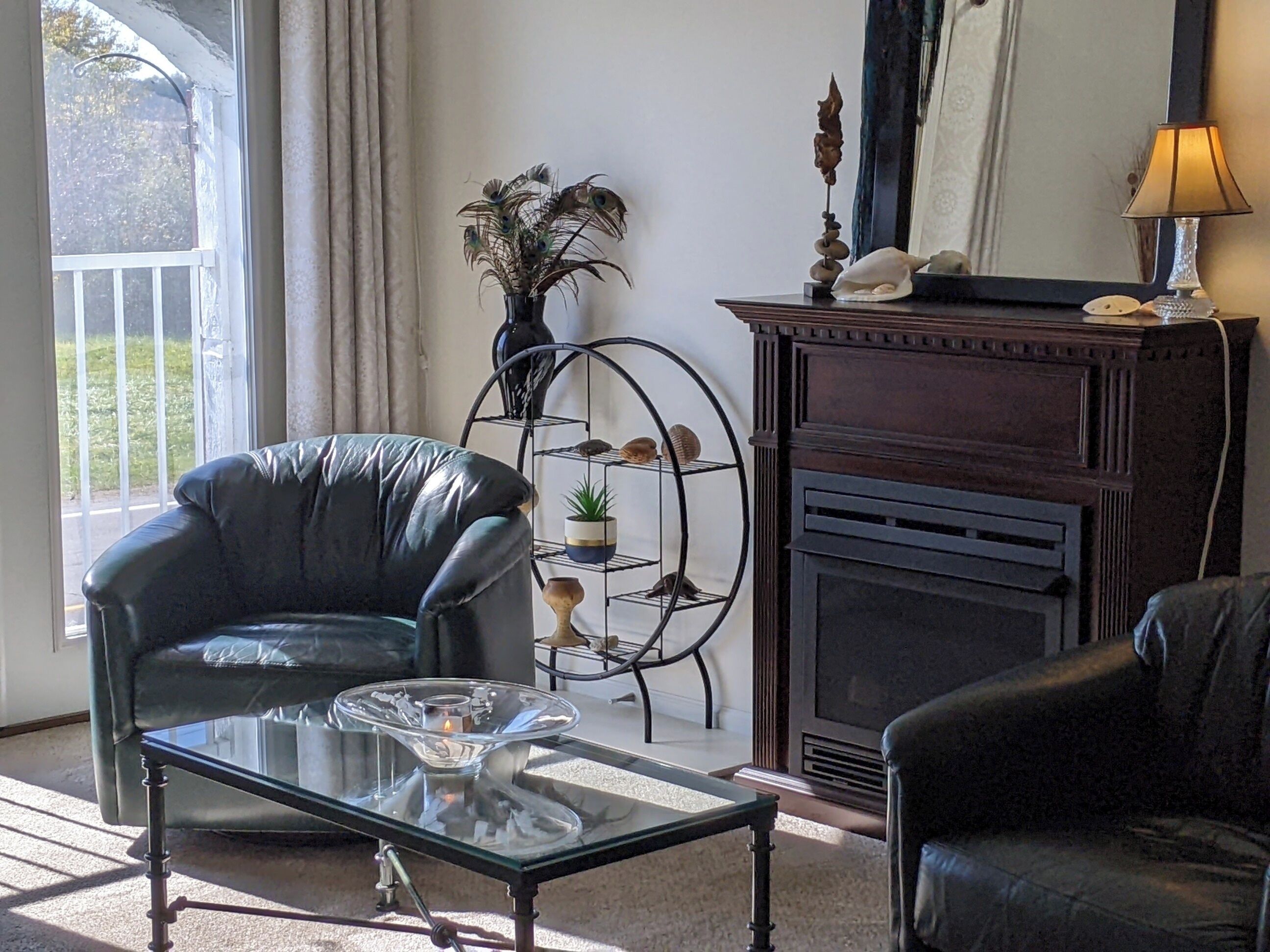 Un salon comprenant un fauteuil en cuir, une table basse en verre, une cheminée et une étagère décorative en métal.